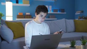 ragazzo con sogni in frantumi, stanco di cattivo e triste testo o e-mail a partire dal il computer portatile. un' ragazzo chi è irritato e frustrato di il cattivo notizia lui sega su il suo il computer portatile mentre studiando a casa. video