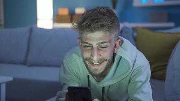 Charismatic and sympathetic young man using phone at home in a happy and fun mood. The sympathetic handsome young man is texting with his girlfriend on his smart phone at home, he is happy and loves. video