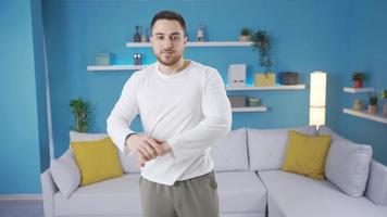 Fitness instructor man doing warm-up and stretching while looking at camera at home. Male fitness trainer doing stretching exercises for his arms and back. Sports trainer. video