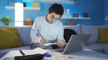 feliz e Diversão Garoto estudando às lar. fofa e simpático Garoto estudando às casa sozinho usando computador portátil, fazendo trabalho de casa. video