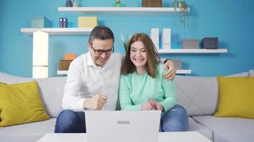 das Vater ist glücklich zu sehen das erfolgreich Ergebnis von seine Tochter auf das Laptop. Vater und Tochter aussehen beim Laptop zusammen und jubeln. Sie sehen das Mädchen Prüfung Ergebnis. video