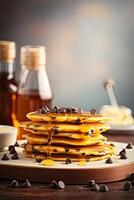 Syrup is poured down and chocolate chips are on top tall stack of golden pancakes layered on a plate with melted butter and syrup dripping down the sides of the stack. . photo