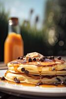 Syrup is poured down and chocolate chips are on top tall stack of golden pancakes layered on a plate with melted butter and syrup dripping down the sides of the stack. . photo