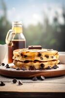 Syrup is poured down and chocolate chips are on top tall stack of golden pancakes layered on a plate with melted butter and syrup dripping down the sides of the stack. . photo