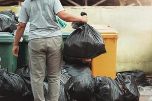 mujer mano participación basura en negro bolso para limpieza en a basura foto