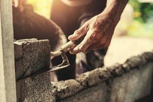 hand of worker plastering cement on brick wall at construction site photo