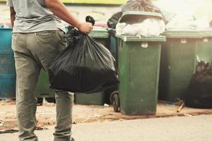 mujer mano participación basura en negro bolso para limpieza en a basura foto