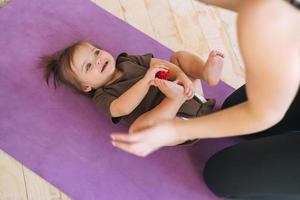 Young woman fit mom with baby girl doing exercises with massage ball on mat at home photo