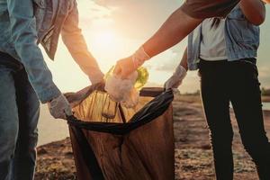 people volunteer keeping garbage plastic and glass bottle into black bag at park river in sunset photo
