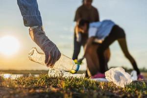 people volunteer keeping garbage plastic bottle into black bag at park river in sunset photo