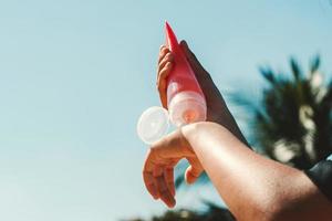 close up young woman applying sunscreen lotion on hand with blue sky background photo