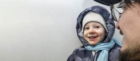 happy boy in a gray jumpsuit, a hat and a blue scarf with abrasions anointed with iodine on his face. child injury. banner with a copy space photo