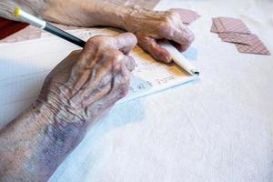 el mano de un mayor mujer con moretones escribir el Puntuación en un tarjeta juego foto