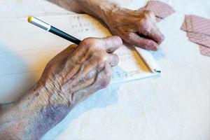 el mano de un mayor mujer con moretones escribir el Puntuación en un tarjeta juego foto