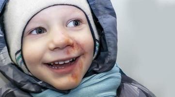 happy boy in a gray jumpsuit, a hat and a blue scarf with abrasions anointed with iodine on his face. child injury. banner with a copy space photo