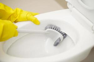 amas de casa utilizar un cepillo a limpiar el baño a eliminar suciedad y tomar cuidado de sanitario mercancía. foto