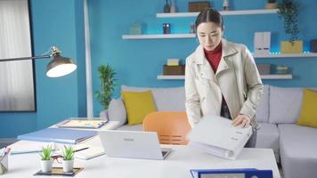 Asian young woman enters the room with a file in her hand and immediately goes to her desk, turns on the laptop and gets to work. video