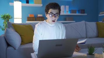 a Garoto quem estudos às casa recebe Boa e Boa notícias, ele é feliz. Garoto levando notas dentro uma caderno regozija-se às a feliz mensagem ou o email a partir de a computador portátil, ele é grato, dele desejos estão garantido. video