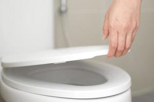 close up hand of a woman closing the lid of a toilet seat. Hygiene and health care concept. photo