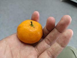 Little orange hold on the bare hand. The photo is suitable to use for fruit background and seller advertising.