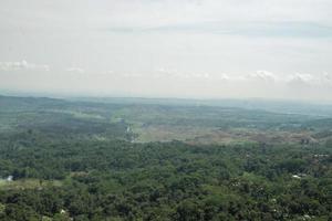 Arial view of peak mountain Central Java Semarang with blue sky and cloudy vibes. The photo is suitable to use for adventure content media, nature poster and forest background.