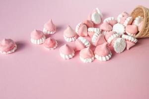 Multicolored pink and white meringues in waffle cookies lie scattered on a pink background photo