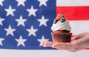 hand holding sweet cupcake with blueberries and strawberry , flag background photo