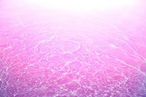 Defocus blurred transparent pink colored clear calm water surface texture with splash, bubble. Shining purple water ripple background. Surface of water in swimming pool. Purple bubble water shine. photo