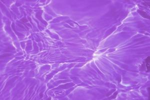 Defocus blurred transparent purple colored clear calm water surface texture with splash, bubble. Shining purple water ripple background. Surface of water in swimming pool. Purple bubble water shine. photo