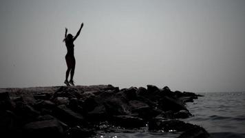 A silhouette of a woman doing aerobics on the ocean beach, jumping and raising her arms up. video