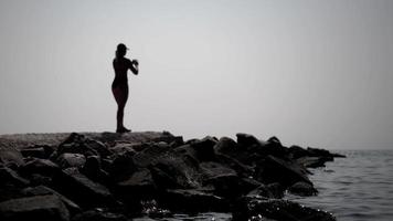 A silhouette of a woman doing sports on the beach, warming up and doing cardio workout. video