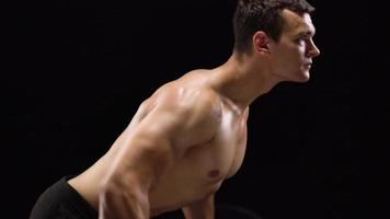 Man is doing exercises with a barbell, training on a black background in the studio. Half body in frame video