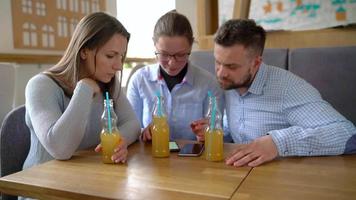 Trois copains asseoir dans une café, boisson jus et avoir amusement communicant video