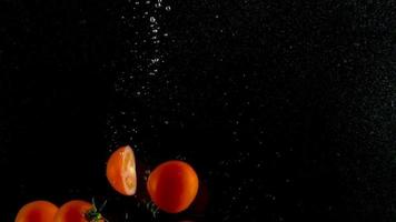 Red tomatoes fall and float in water, black background, slow motion video