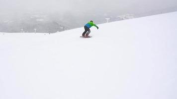 View from height to man is riding a snowboard on a snow-covered field on a cable behind a car video