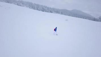 vol plus de le solitaire touristique fille en marchant le long de le Haut de une Montagne couvert avec neige. inconfortable hostile hiver temps. video