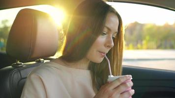 Beautiful cheerful girl sits in the car, drinks coffee and laughs video