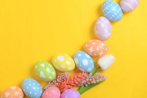 Happy Easter holiday greeting card design concept. Colorful Easter Eggs and spring flowers on yellow background. Flat lay, top view, copy space. photo