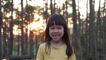 Porträt von ein glücklich lächelnd Kind draußen im das Wind gegen natürlich Hintergrund und warm Sonnenlicht im Park. video