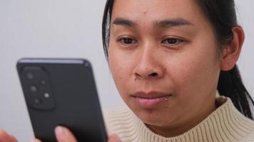 portrait de asiatique femme en portant mobile téléphone, en train de lire mal message, sentiment triste et pleurs. dérangé Jeune femme séance à Accueil en portant une téléphone intelligent dans sa main reçoit une message avec mal nouvelles. video