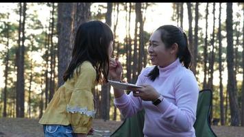 contento madre y niños picnic sentar por estufa cerca tienda y parrilla un parilla en pino bosque, comiendo y tener conversación. contento familia en vacaciones en naturaleza. video