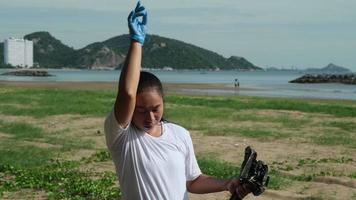 asiatisch Frau im Handschuhe ist abwischen Schweiß auf ihr Gesicht müde von Reinigung das Strand. Frau Freiwillige Portion zu behalten Natur sauber und pflücken oben das Müll von ein sandig Ufer. Erde Tag Konzept video