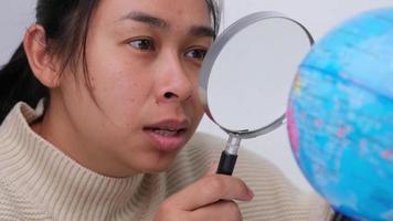 Portrait of tourist woman holding and looking through magnifying glass on globe isolated on white background. video