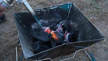 giovane escursionista uomo Tenere un' gas torcia bruciatore carbone su il fornello. un' infiammabile idrocarburo gas licenziare su bruciare legno duro nero carbone per grigliate cibo preparazione. viaggio e stile di vita concetto. video