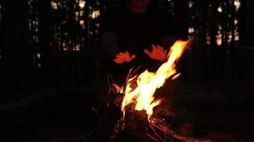 Young hiker kindling a mountain fire and warming up near the campfire at night. Traveler man lighting a fire in the camp near the tent while spending time in the nature. Travel and lifestyle concept. video