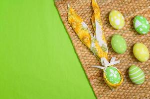 Happy Easter holiday greeting card design concept. Colorful Easter Eggs and spring flowers on pastel green background. Flat lay, top view, copy space. photo