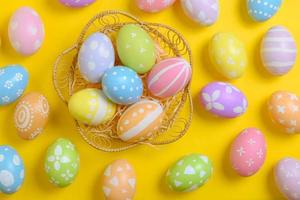 Happy easter celebration holiday. colourful pastel painted eggs in wicker basket nest decoration on a yellow background. Seasonal greeting gift card concept. Top view, flat lay, copy space. photo