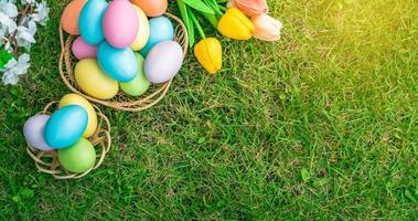 Happy Easter holiday greeting card concept. Colorful Easter Eggs and spring flowers on green grasses background. Flat lay, top view, copy space. photo