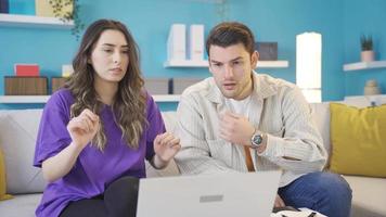 Happy lovers get sad. Young lovers getting bad news at home on laptop. The young couple working at home on the laptop are sad and disappointed to receive bad news. video