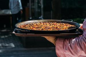 Waiter holding a giant Spanish paella dish outside a restaurant terrace photo